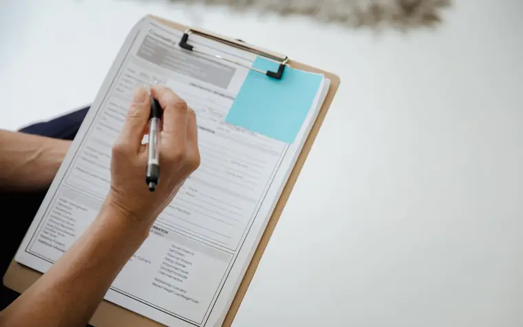A hand completing a form on a clipboard