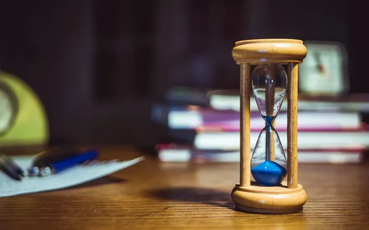 An hourglass sitting on a desk next to a stack of books