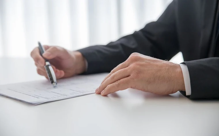A man in a suit signing a document at his desk