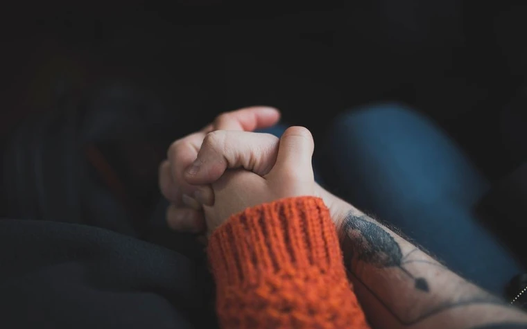 Two hands clasped together, one sleeve pulled up under a warm sweater