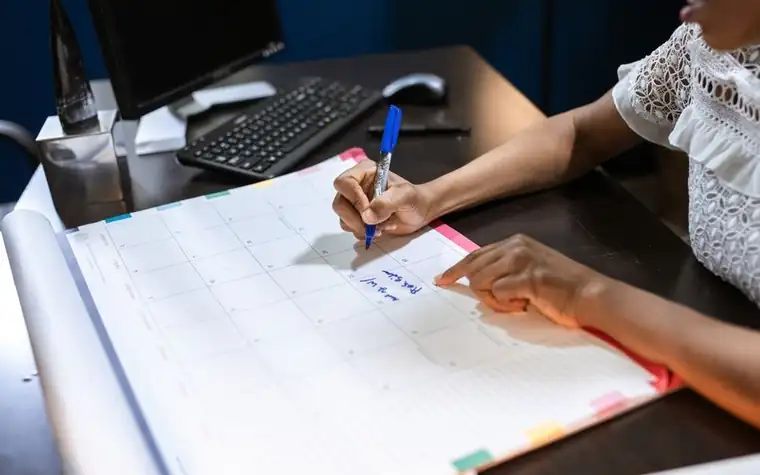 책상 위 달력에 파란 펜으로 일정을 적는 손