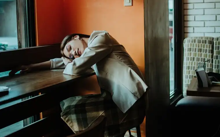 A woman napping with her head on a wooden cafe table