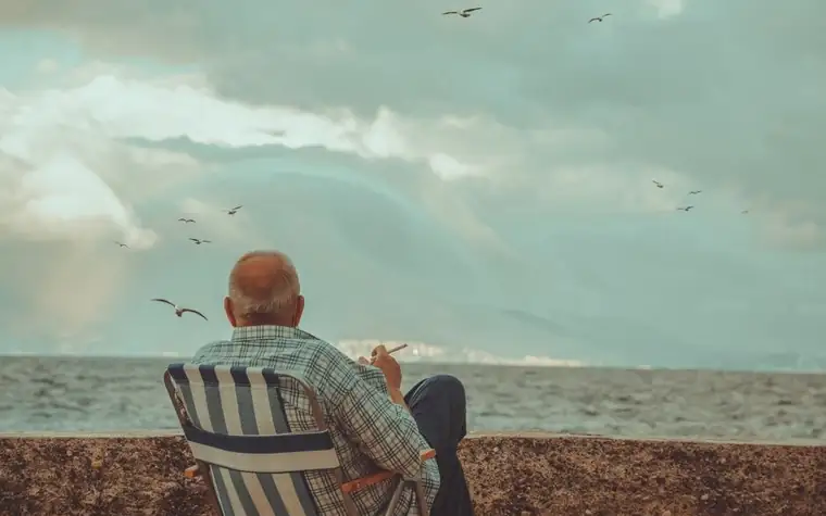 An older man seen from behind sitting on a beach chair and looking out at the sea