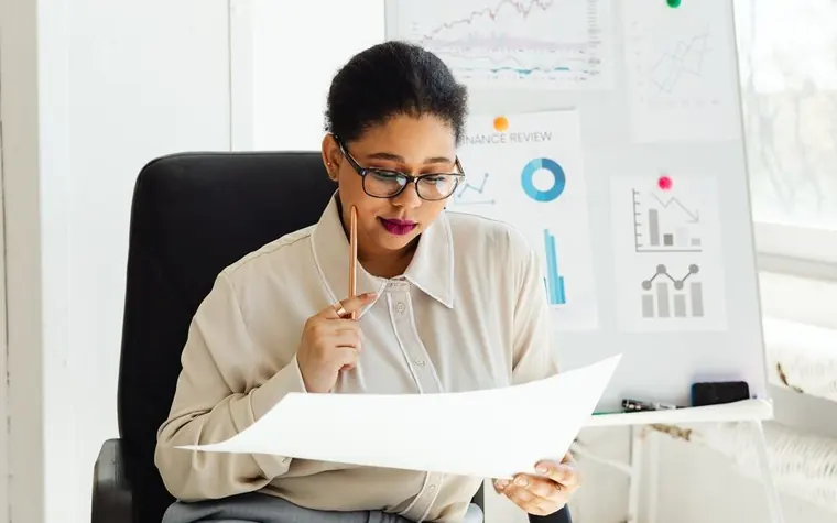 A woman with glasses sitting in a chair and looking over a document