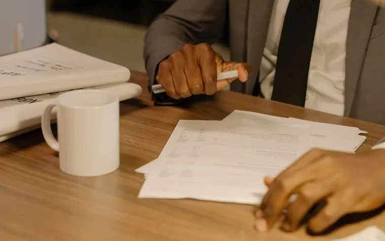 A hand reviewing a contract and documents on an office desk