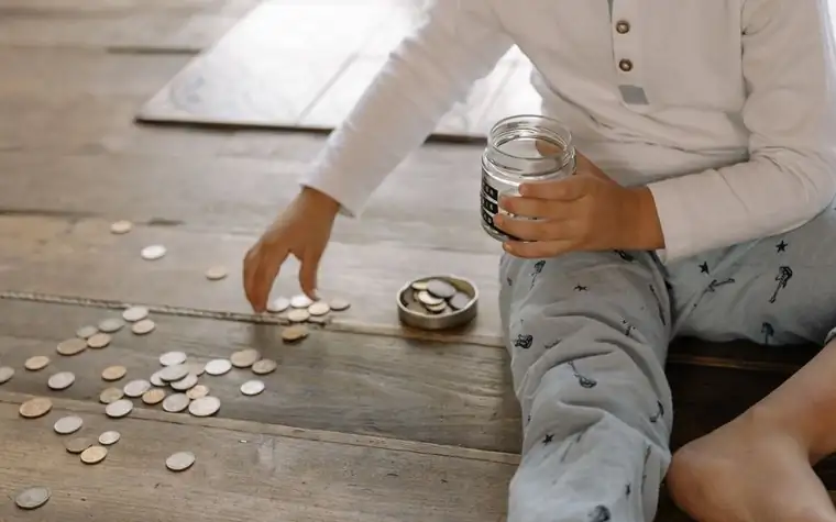 A child collecting coins into a jar on a wooden floor