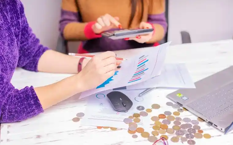 Two people reviewing financial charts with a laptop and coins