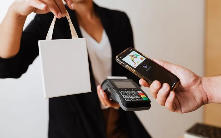 A hand paying with a card on a smartphone at a store counter
