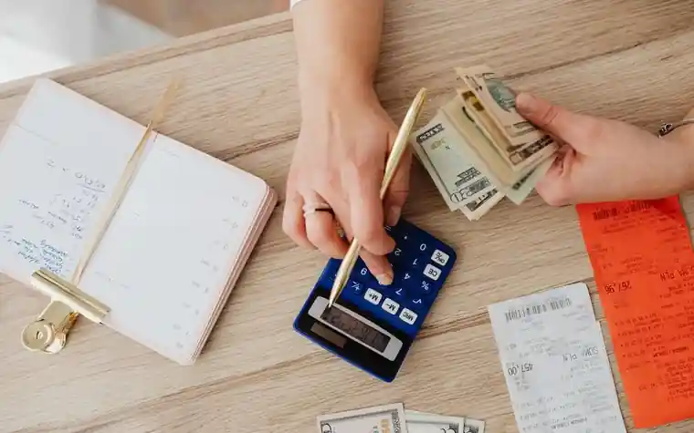 Hands using a calculator with cash and receipts to track a budget