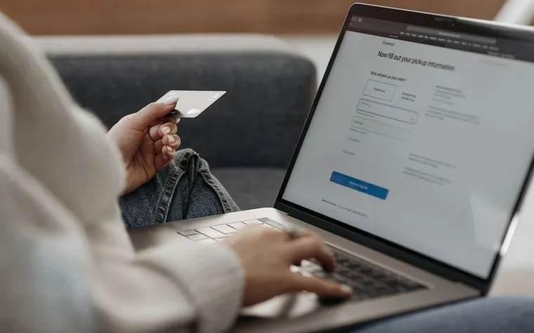 A hand holding a card while checking an online banking screen on a laptop