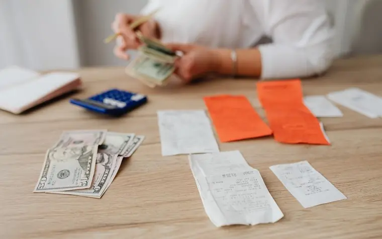 A calculator, cash, and receipts laid out on a desk