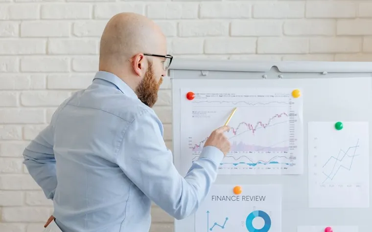 A man pointing at a stock chart pinned to a whiteboard while explaining it
