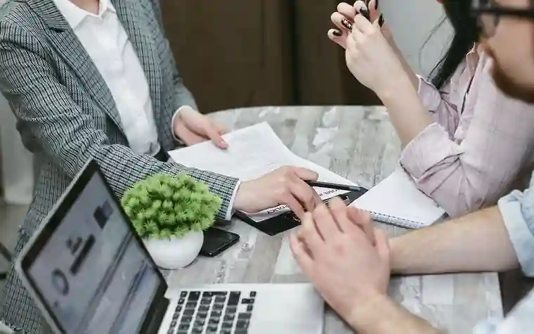 People wearing masks talking at a meeting table with a laptop and documents