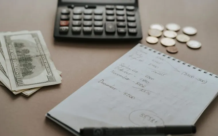 A calculator, cash, and coins on a desk next to financial notes