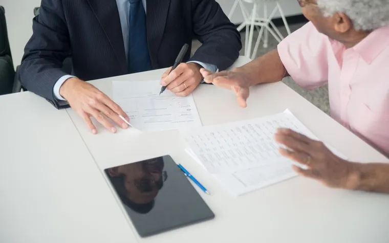 An advisor in a suit signing documents while consulting with a client