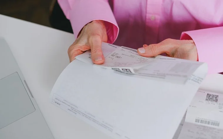 A person in a pink shirt flipping through bills and receipts by hand