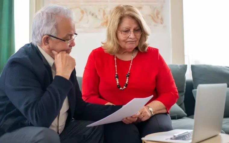 An older couple looking over documents together on a living room sofa