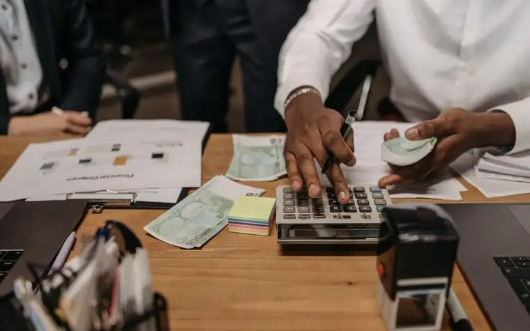A person in business attire working with a calculator and paperwork at a desk
