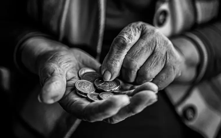 An elderly hand holding a pile of coins, in black and white
