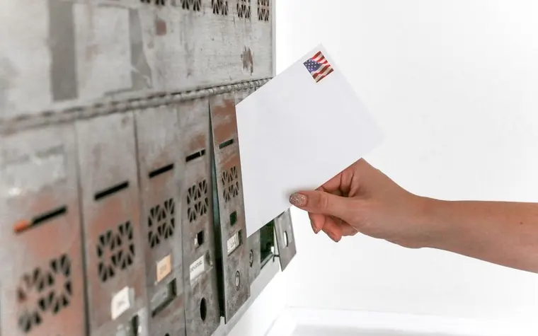 A hand slipping a stamped envelope into a mailbox, symbolizing a tax notice arriving in the mail