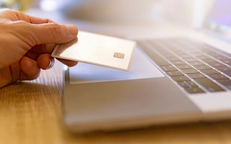 A hand holding a credit card in front of a laptop, paying a tax bill online by card