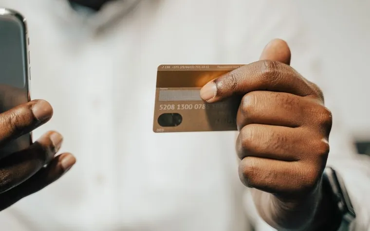 A hand holding a phone and a credit card together