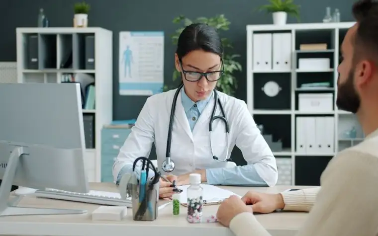 A doctor and patient sitting across a clinic desk, seen from behind the patient