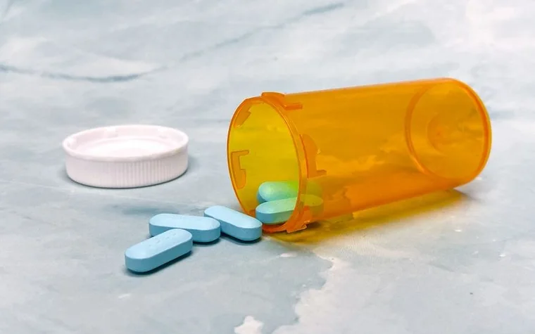 Blue and white pills spilling out of an orange prescription bottle