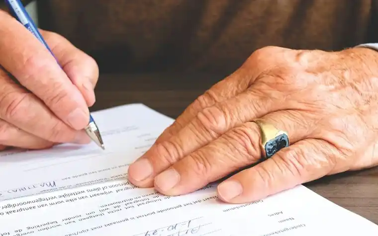 An elderly person's hand signing a support application form
