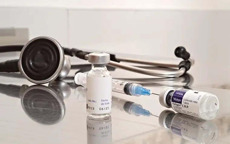 A vaccine vial, syringe and stethoscope on a table