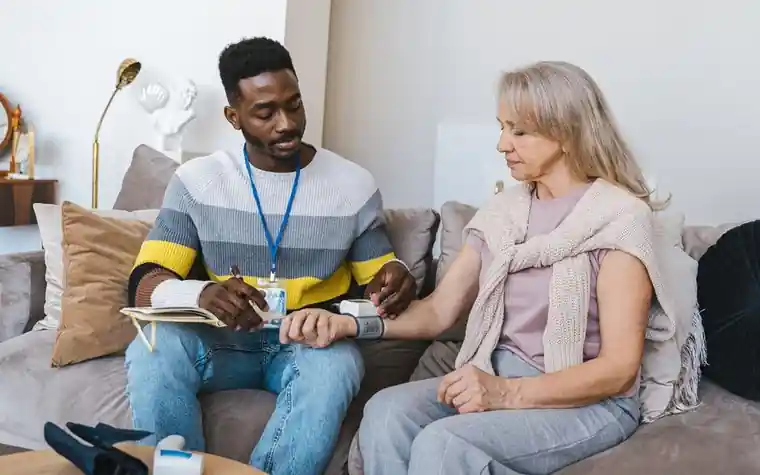 Checking an older woman's blood pressure on a living room sofa