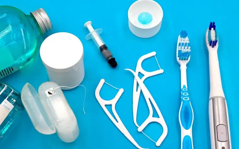 A toothbrush, floss and oral care products laid out on a blue surface
