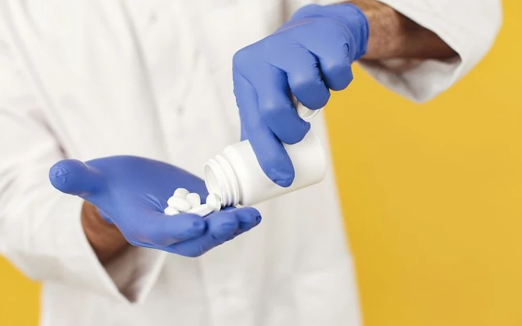 A gloved hand pouring pills from a bottle into the palm