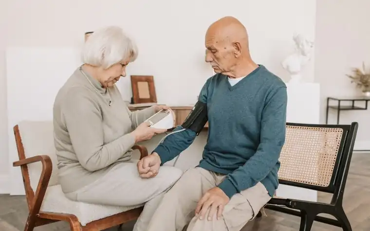 An older couple at home, one with a cuff on the arm taking a blood pressure reading