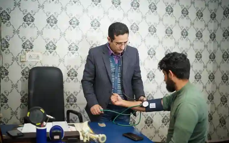 A doctor wrapping a cuff around a patient's arm to measure blood pressure in an examination room