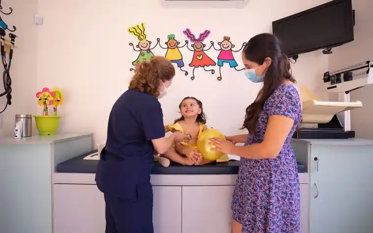 A nurse checking a child on an examination table in a pediatric clinic while a parent stands beside them