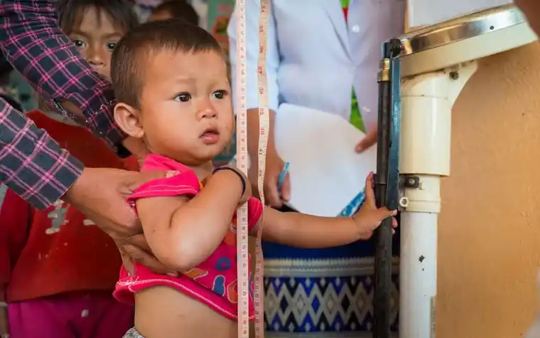 A young child standing beside a scale while height and weight are measured