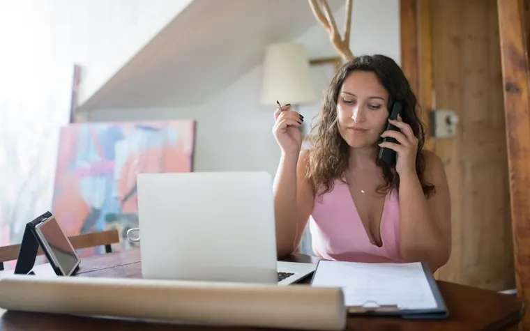 A woman on the phone in front of a laptop, checking paperwork
