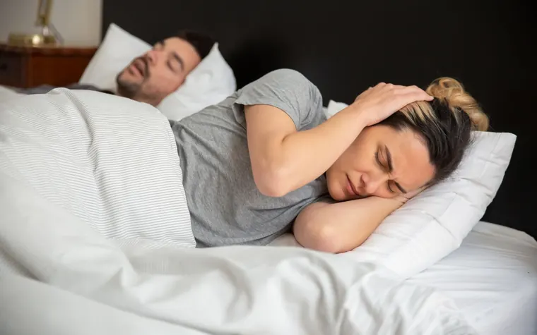 A person covering their ears in bed at night because of noise