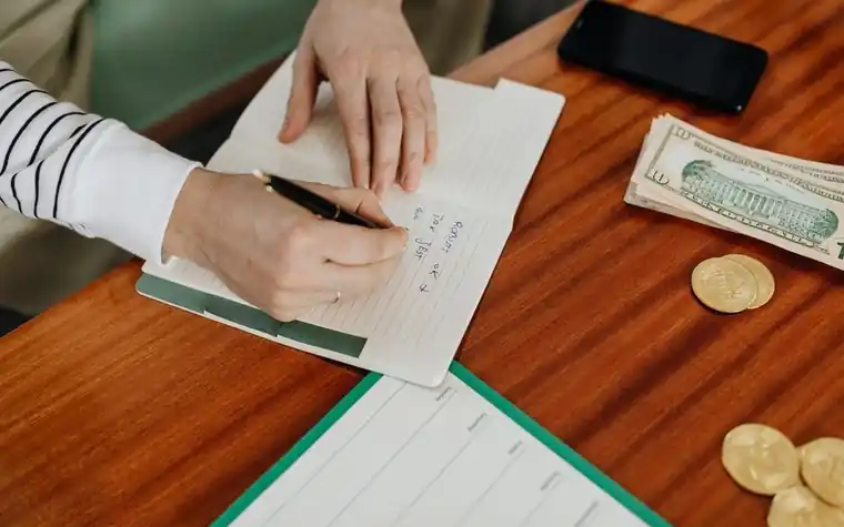 A hand writing a budget next to receipts and cash