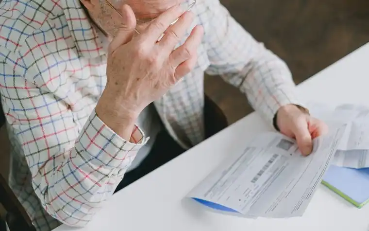 Elderly man checking a bill in his hand at the kitchen table