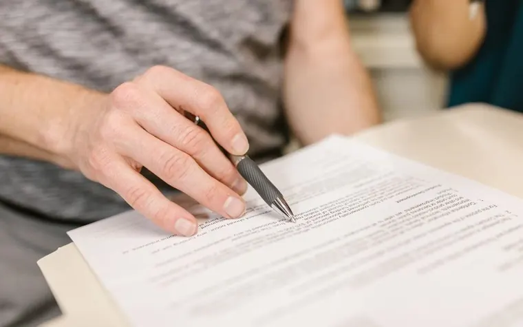 Hand reviewing a contract and documents spread on a desk