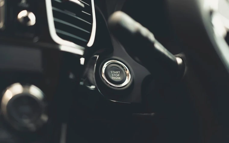 A dark car interior with the dashboard lit beside the engine start button