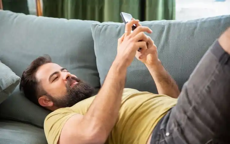 A man lying on a sofa looking at his smartphone screen
