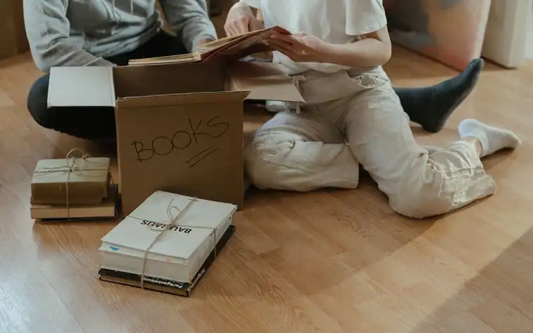 Two people sitting on the floor sorting a box of books