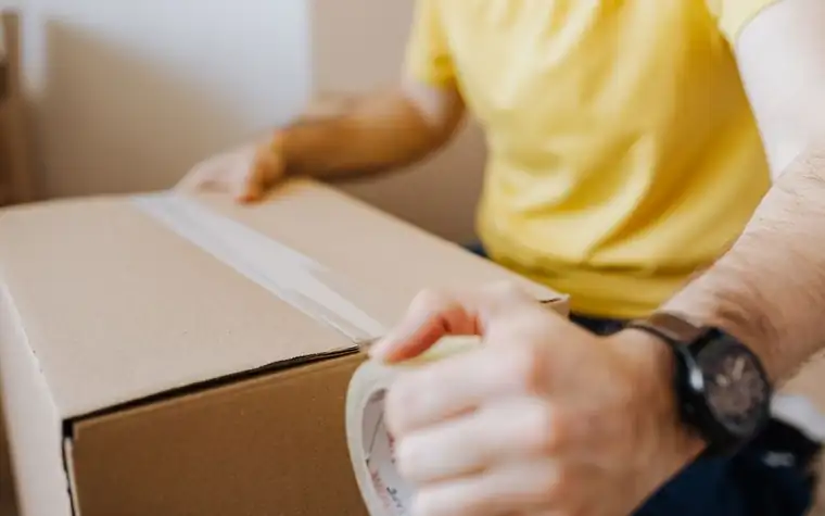 A hand applying packing tape to a box