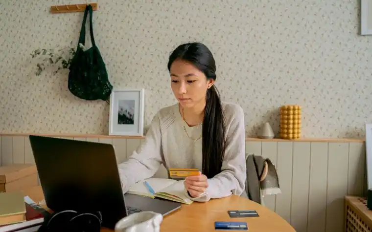 A woman holding a credit card in front of a laptop, checking her payment history