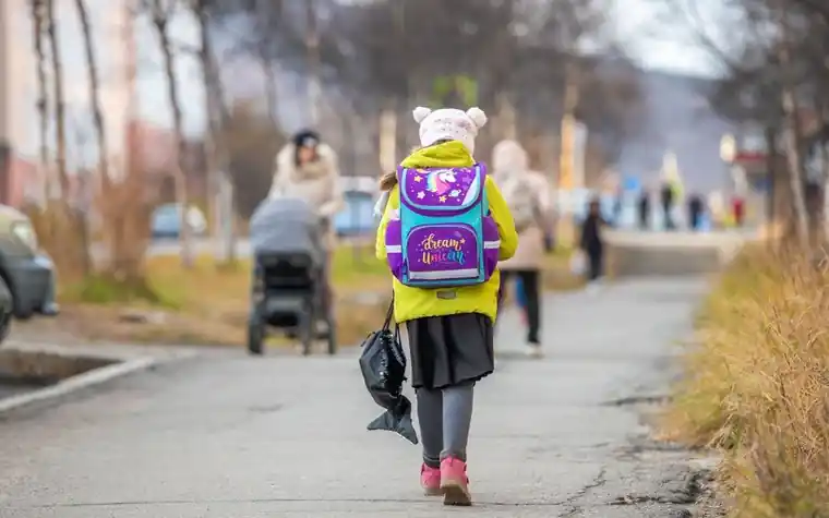 The back of a young student walking down a street wearing a school backpack