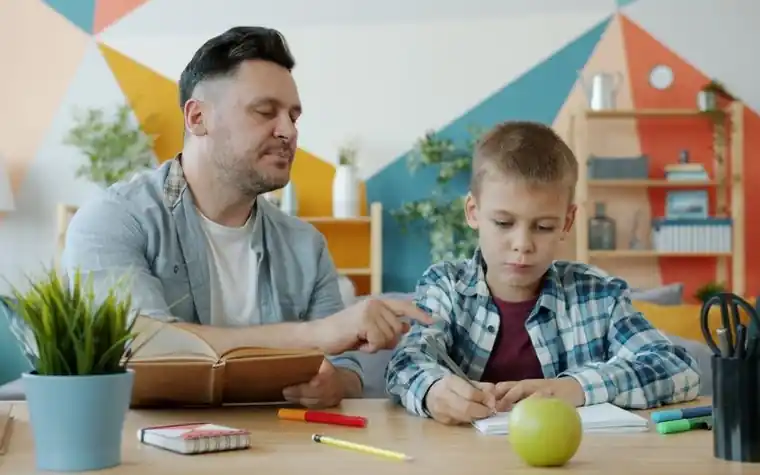 A father sitting beside his son and helping with his homework