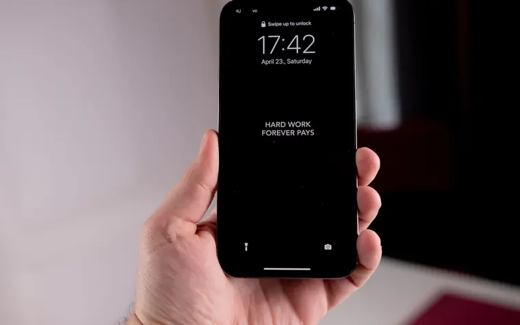 A hand holding a smartphone showing its lock screen